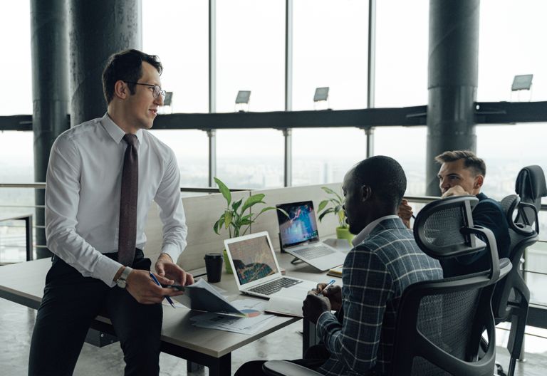 Three men engaged in a business meeting in a modern office setting with laptops and documents.